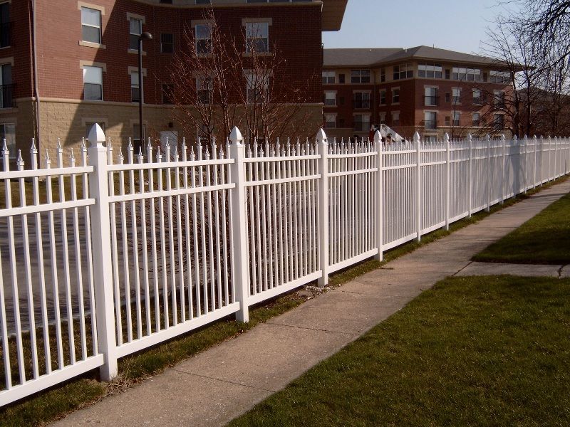 White metal fence along a sidewalk with buildings in the background.