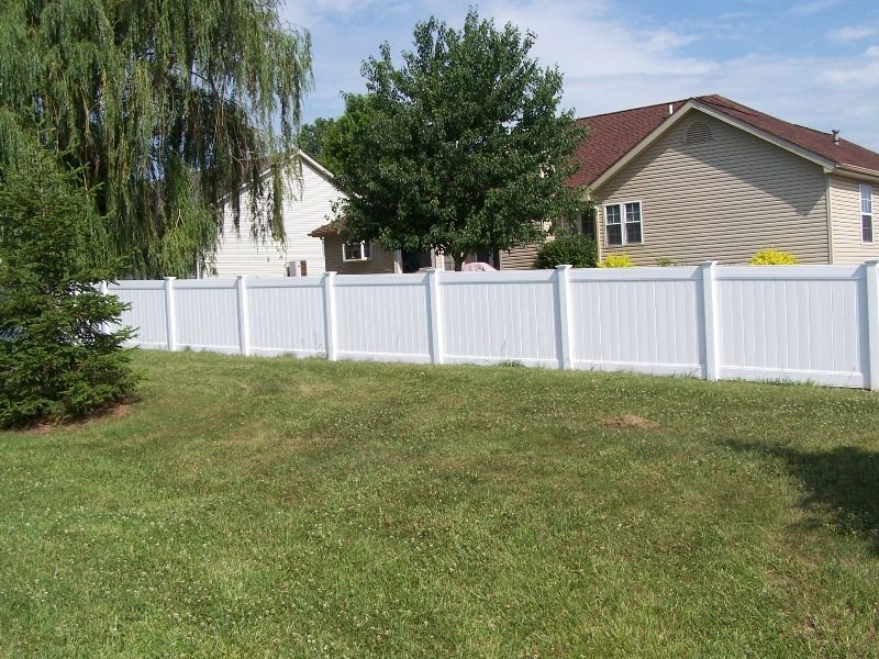 White vinyl fence bordering a grassy lawn in front of two houses.