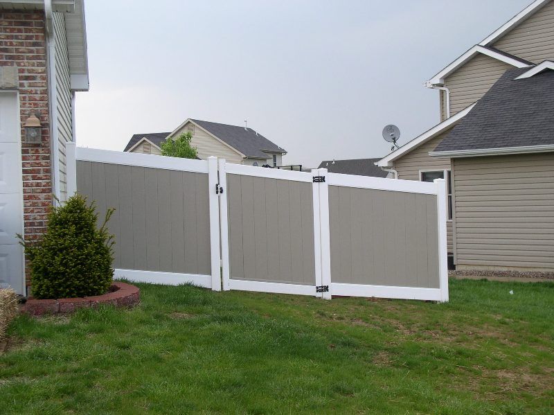 A section of a gray and white privacy fence separating two houses with a small green bush in front.