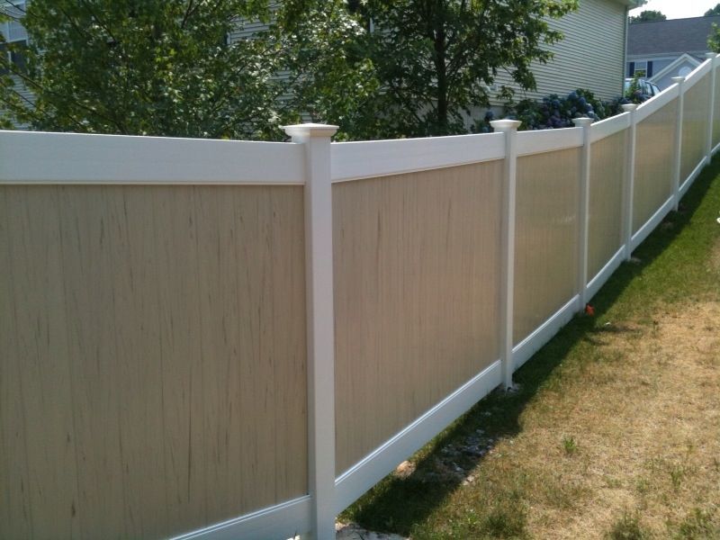 Beige and white vinyl privacy fence in a sunny yard.