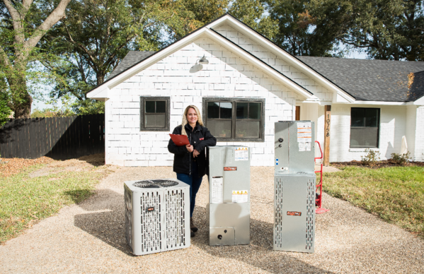 A woman is standing in front of a white house holding a clipboard.