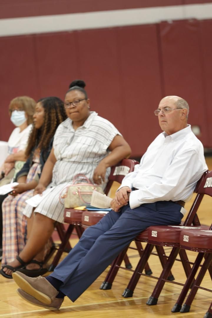 A group of people are sitting on folding chairs in a gym