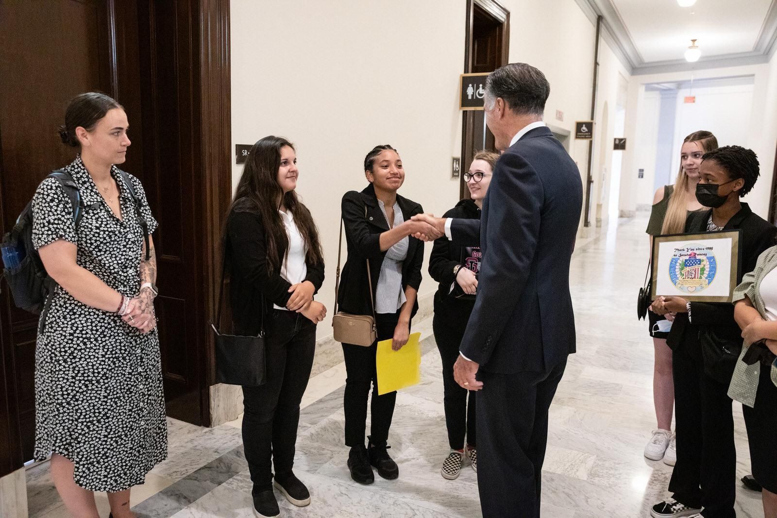 A group of people are standing in a hallway talking to a man in a suit