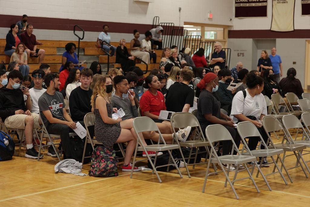 A group of people are sitting in folding chairs in a gym
