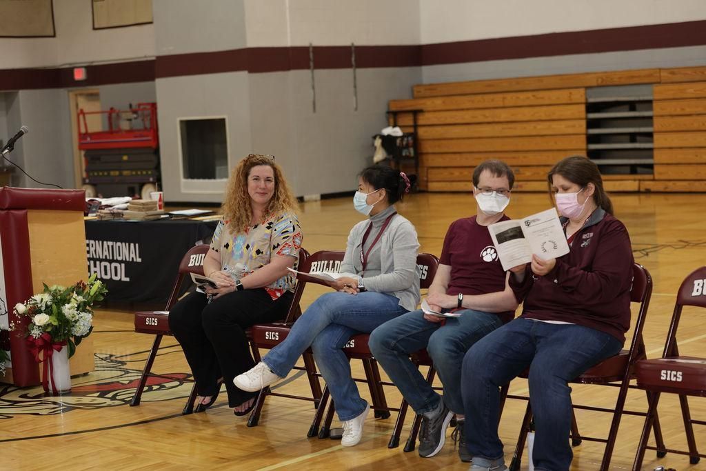 A group of people wearing face masks sit in chairs in a gym