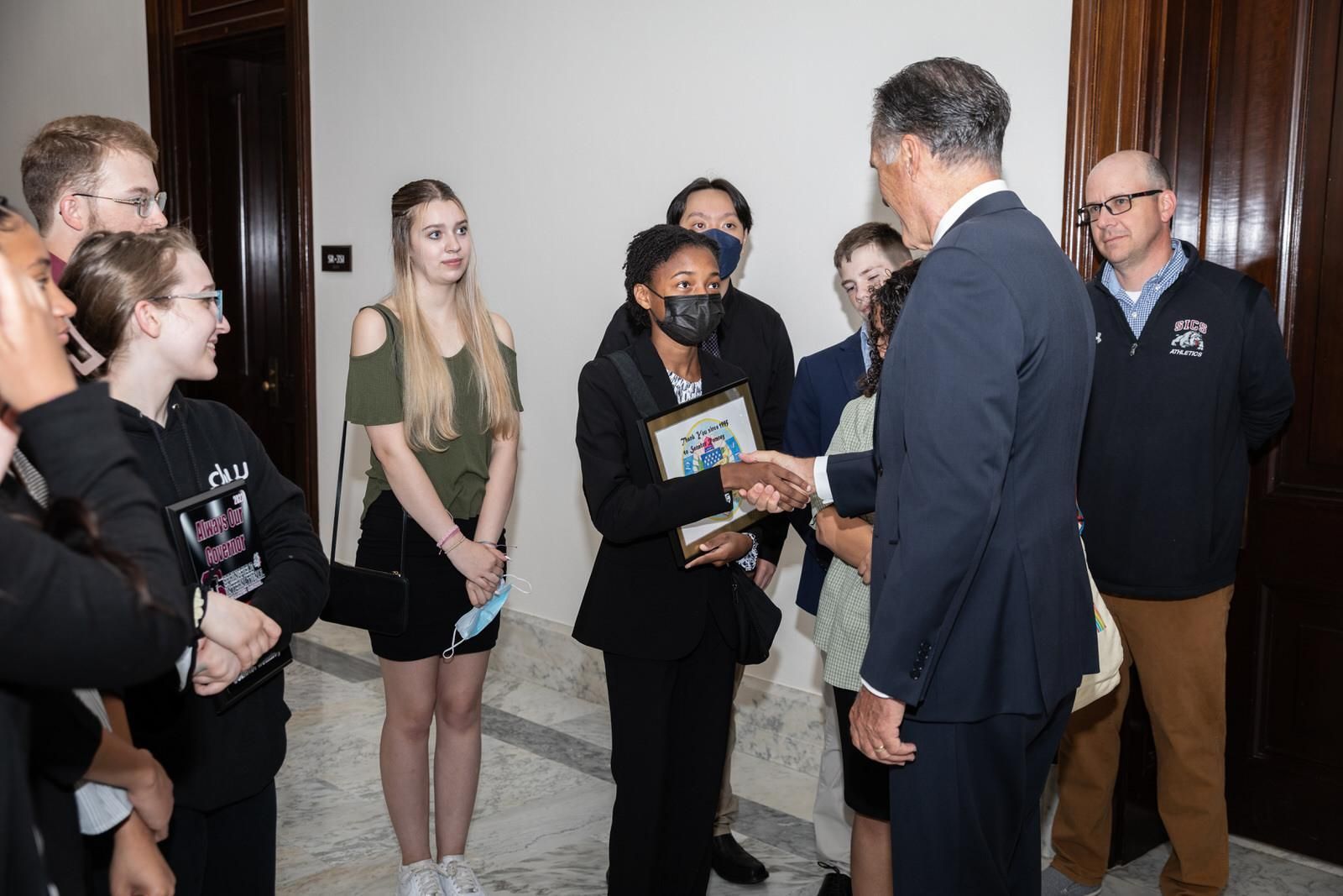 A group of people are standing around a man in a suit shaking hands