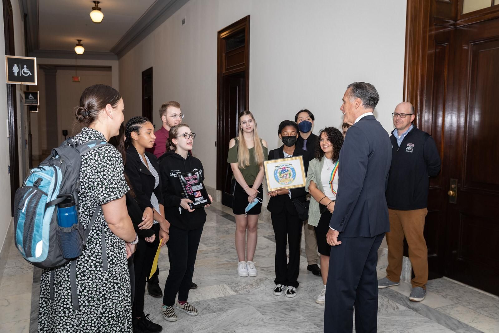 A group of people are standing in a hallway talking to a man in a suit