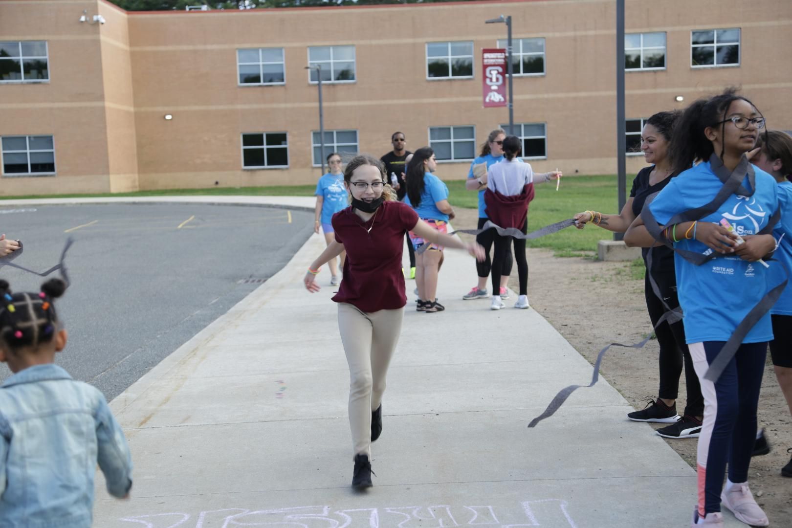 A girl in a blue shirt is running down a sidewalk