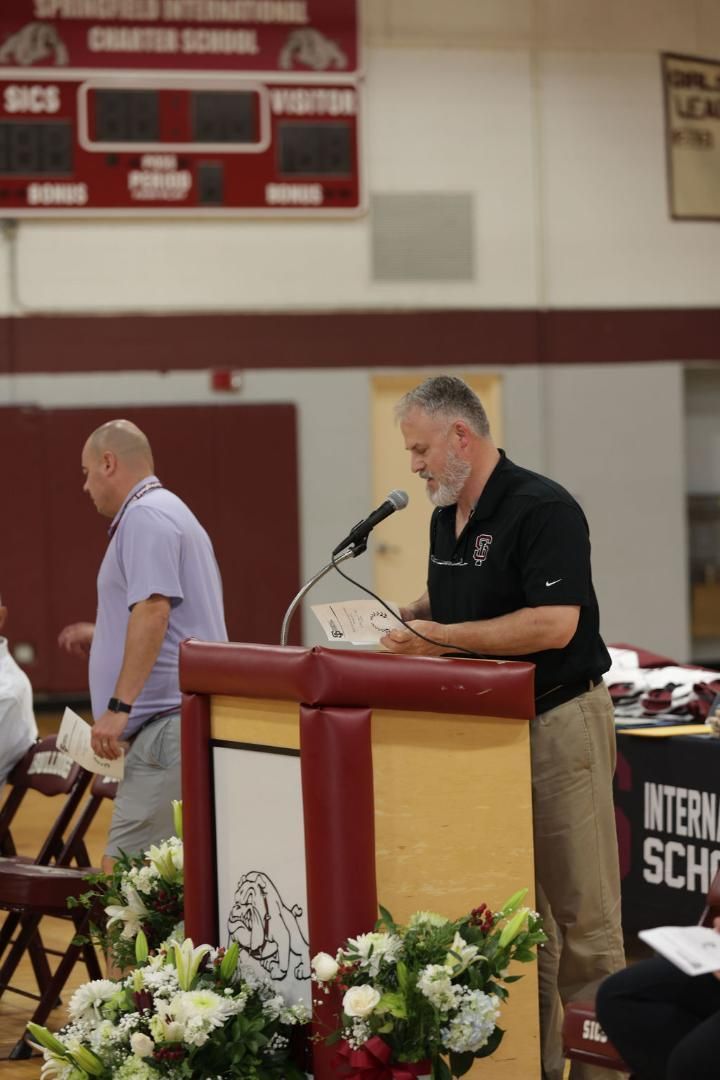 A man stands at a podium in front of a scoreboard that says sics
