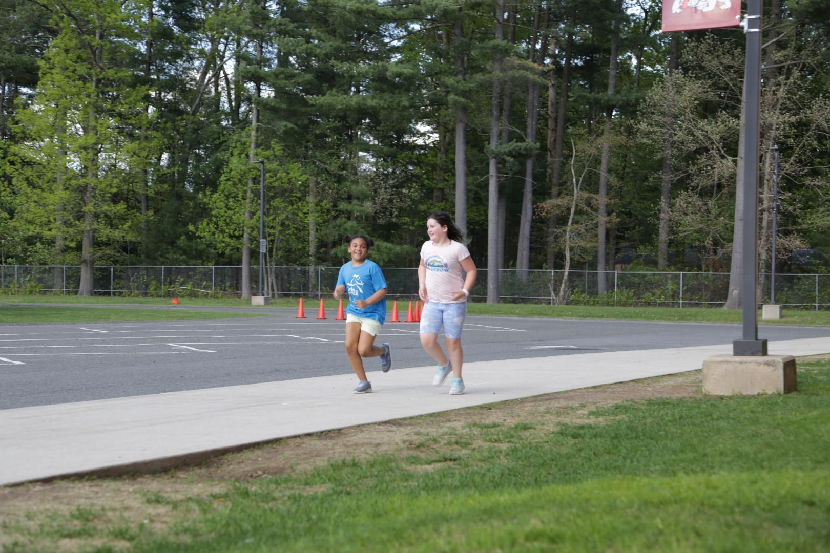 Two girls are running on a sidewalk in front of a sign that says ' emerson '