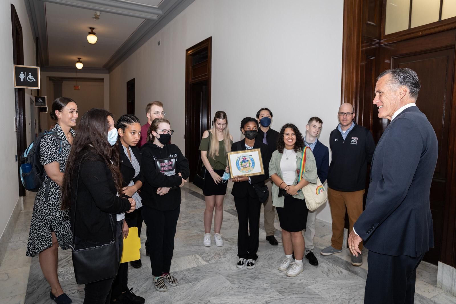 A group of people are standing in a hallway talking to a man in a suit