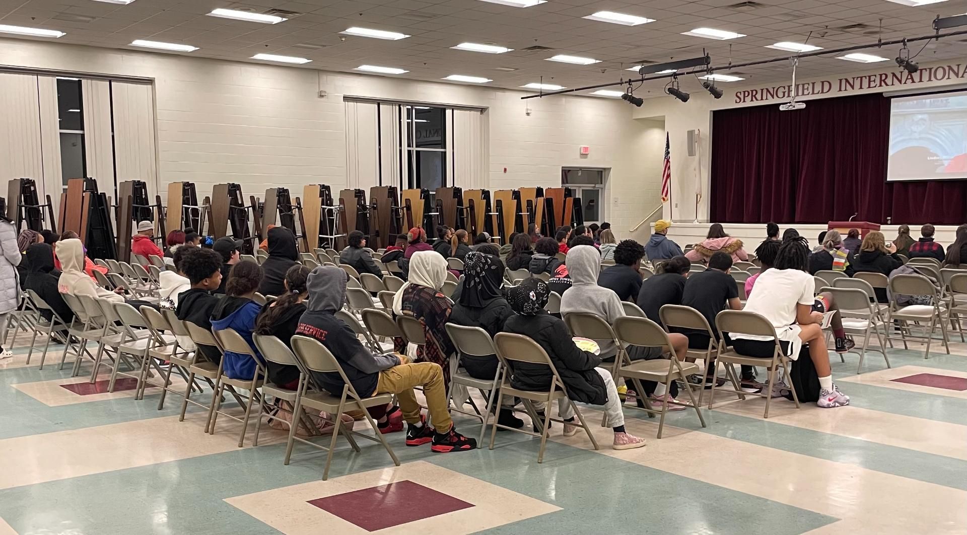 A large group of people are sitting in chairs in a large room