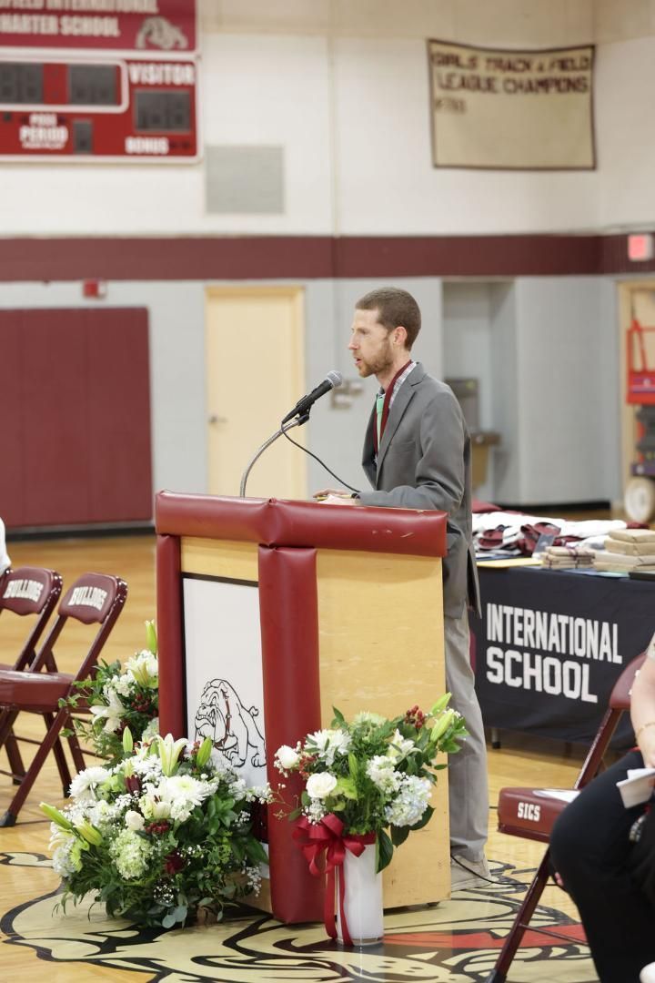 A man stands at a podium in front of a sign that says international school