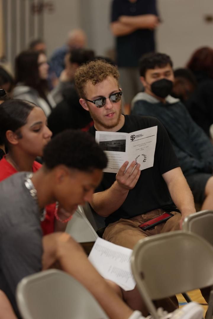 A man wearing sunglasses is sitting in a chair reading a book