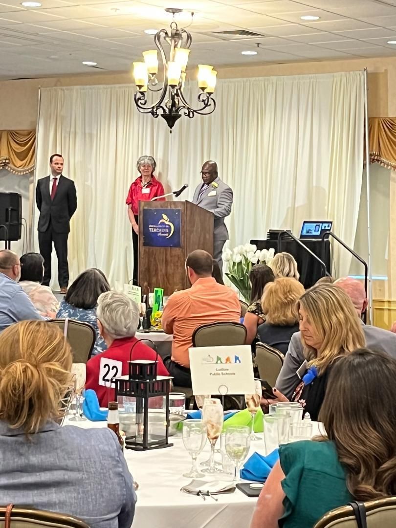 A group of people are sitting at tables in a room with a man standing at a podium giving a speech.