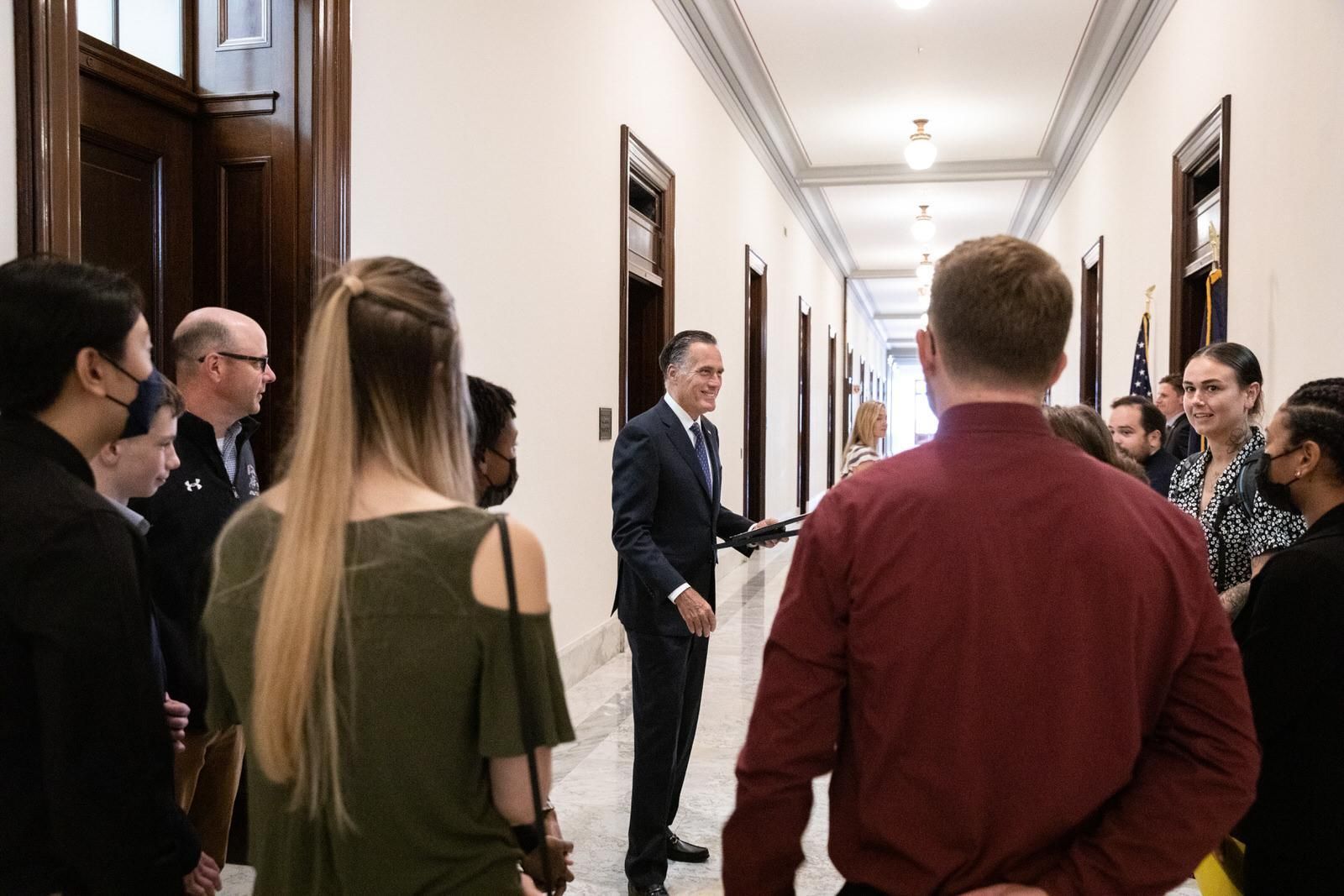 A man in a suit is talking to a group of people in a hallway