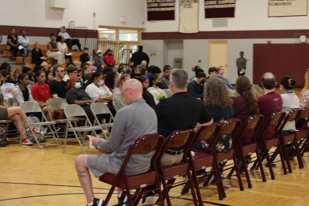 A group of people are sitting in folding chairs in a gym