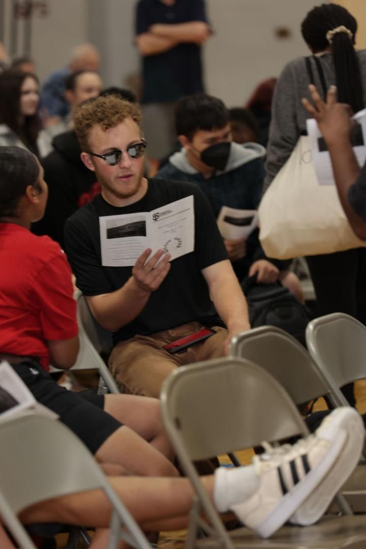 A man wearing sunglasses sits in a chair reading a book