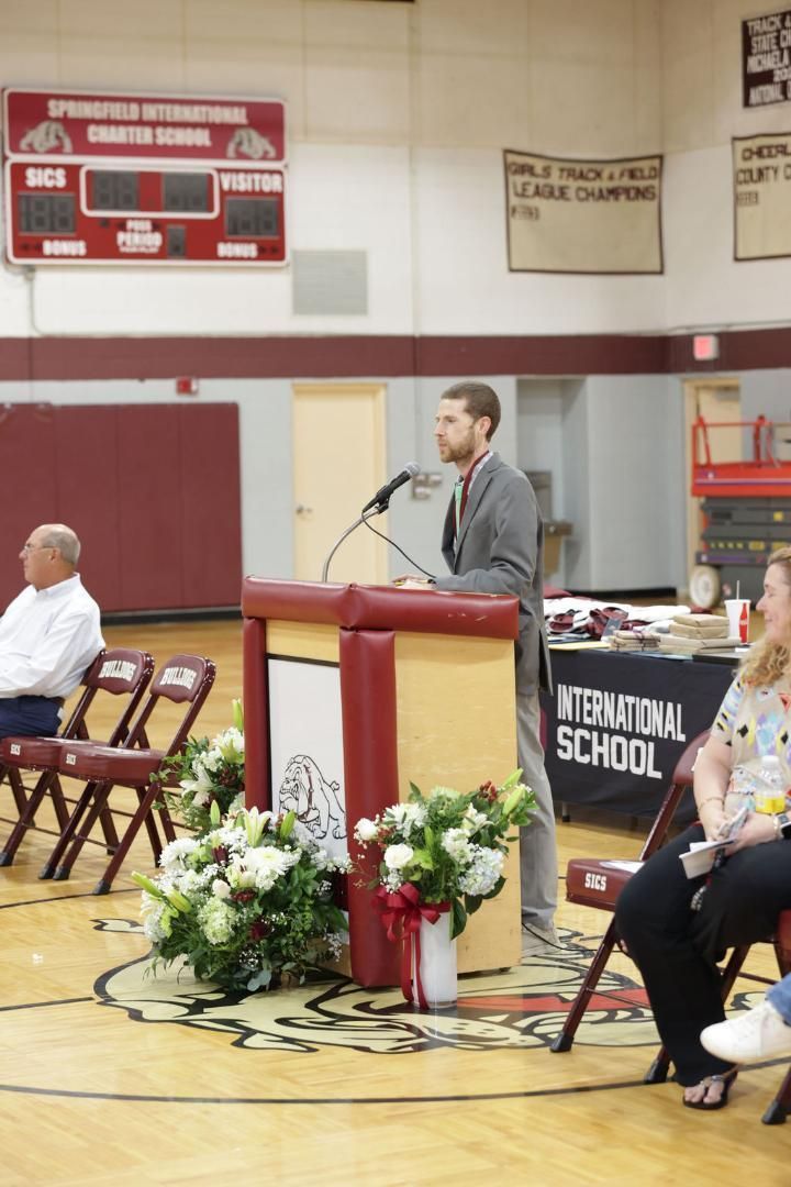 A man stands at a podium in front of a sign that says memorial school