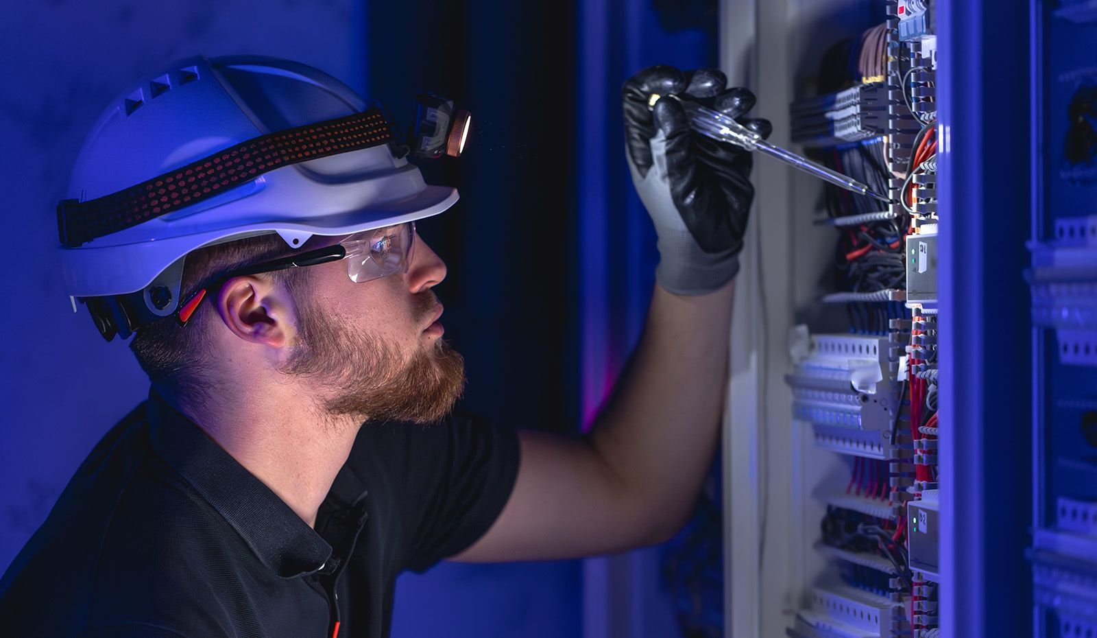 AMS electrician working on electrical panel upgrades, wearing safety hat and glasses and headlamp for efficient electrical services.