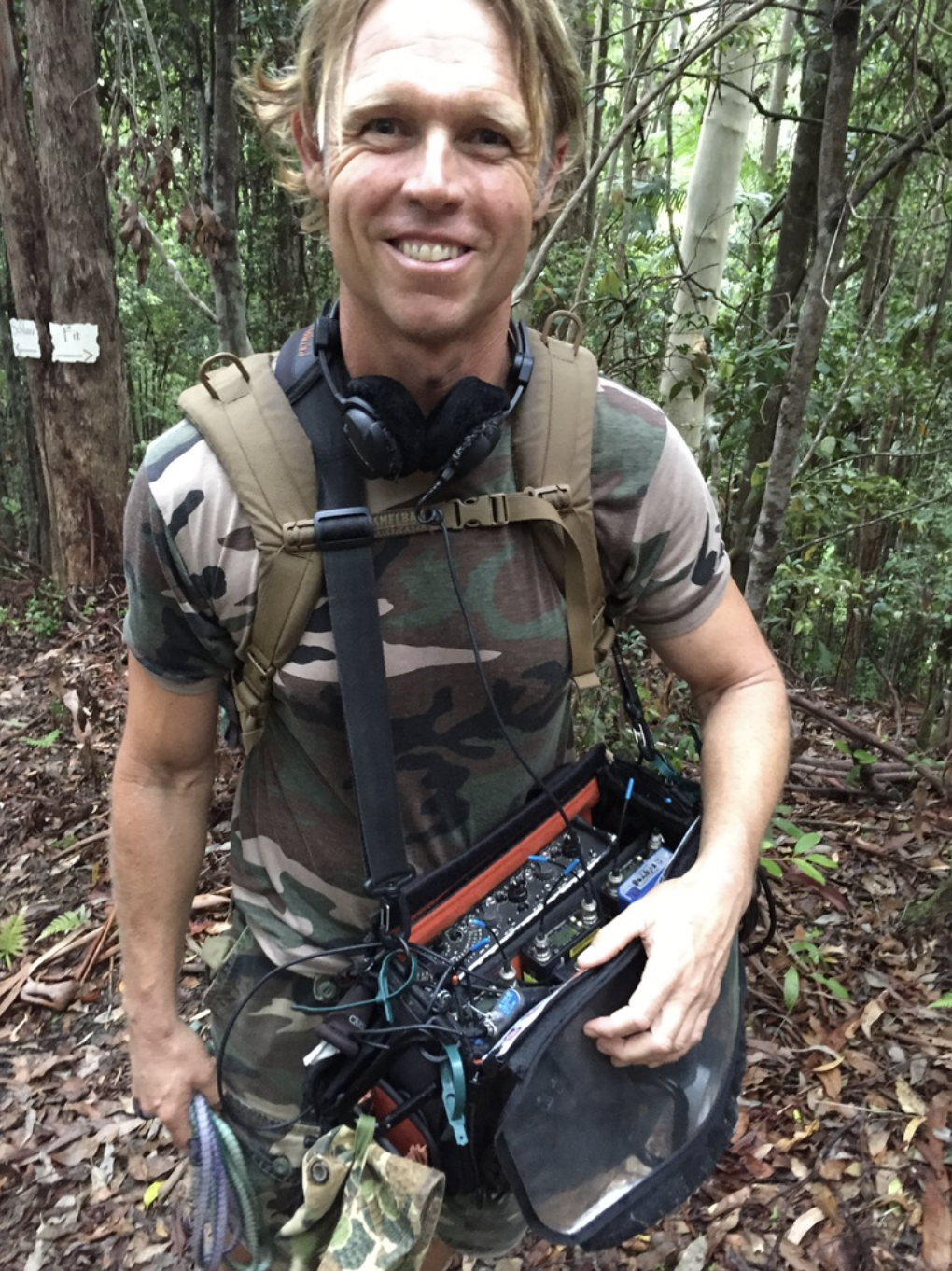 A man in a camouflage shirt is holding a radio in the woods.