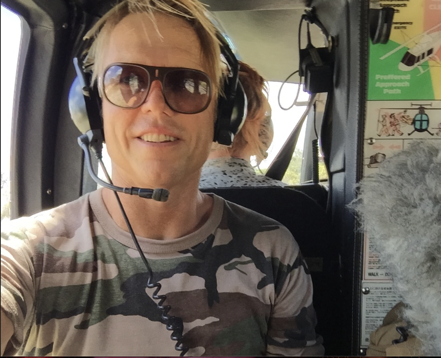 A man wearing sunglasses and headphones takes a selfie in a helicopter