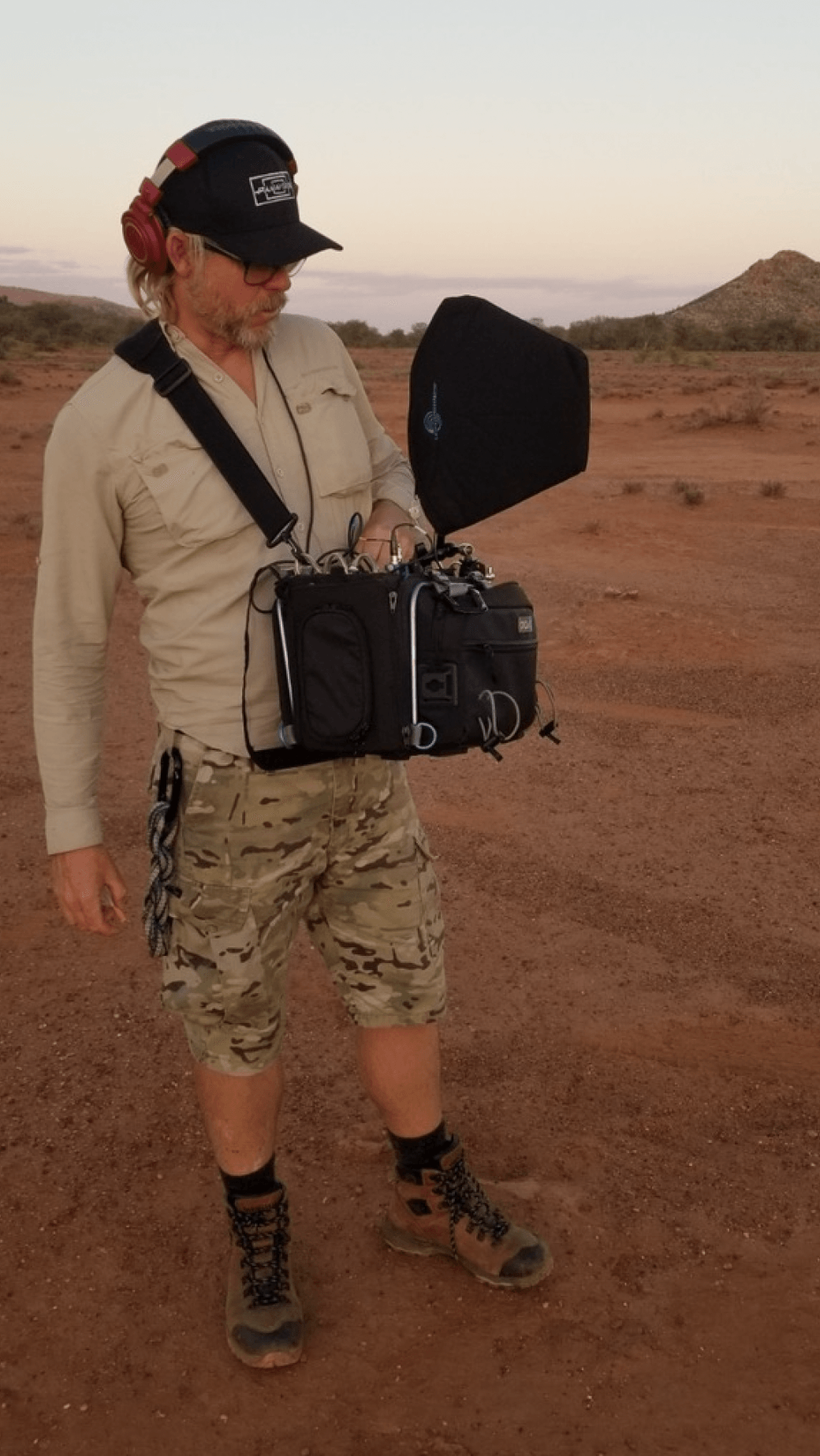 A man is standing in the middle of a desert holding a camera.