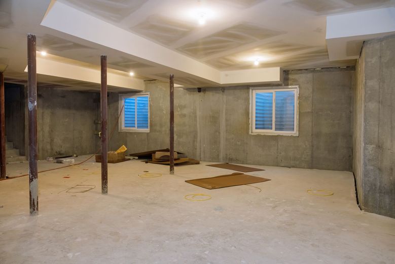 Unfinished basement with concrete walls, support beams, and two windows with blue light.