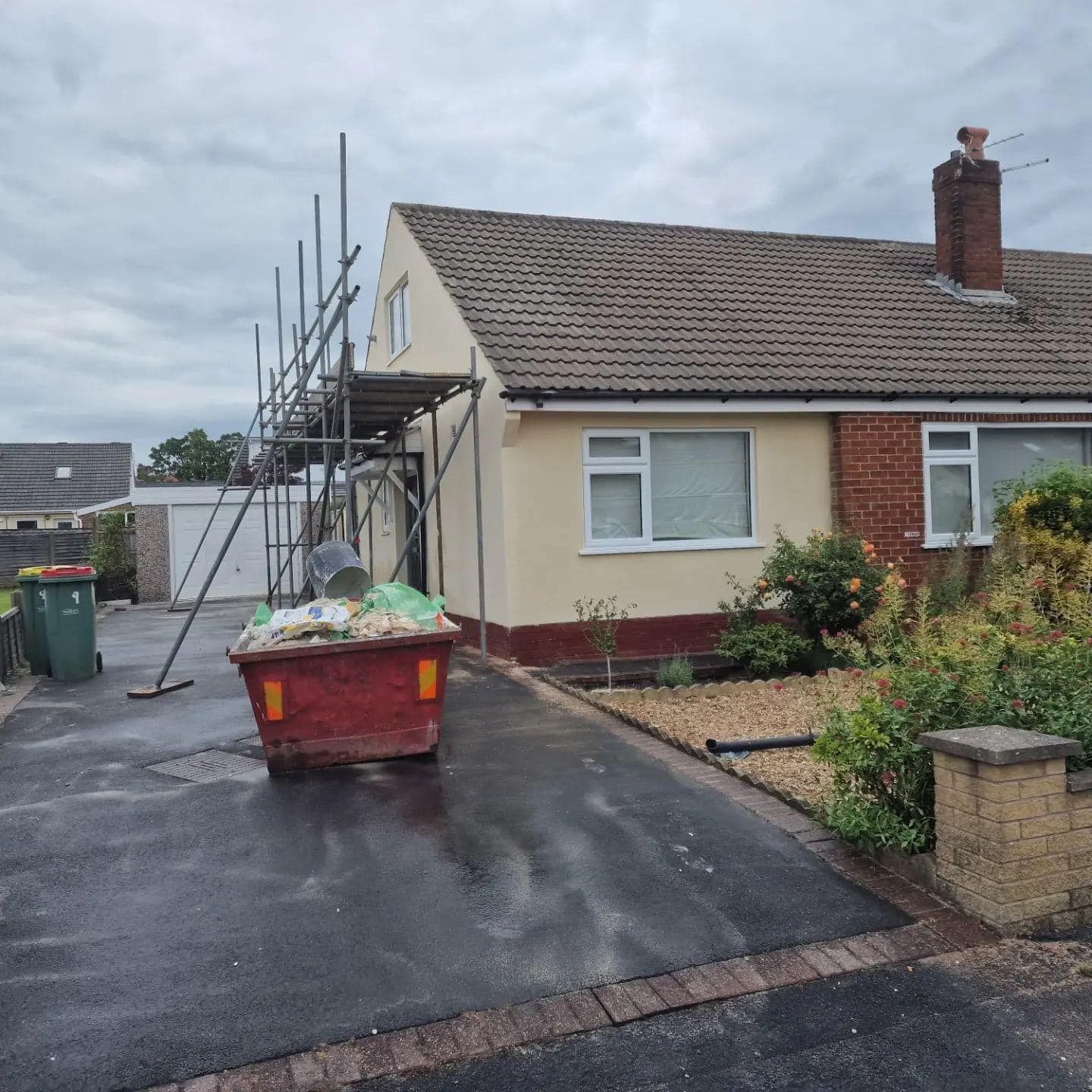 Bungalow under renovation, scaffolding, skip, and driveway visible. Cloudy day.