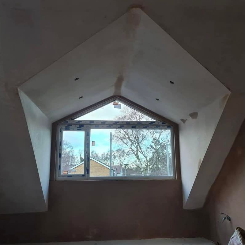 Window in a newly plastered, angular ceiling. Exterior view through the window.