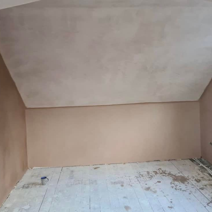 Room with freshly plastered walls and ceiling; bare wooden floor.