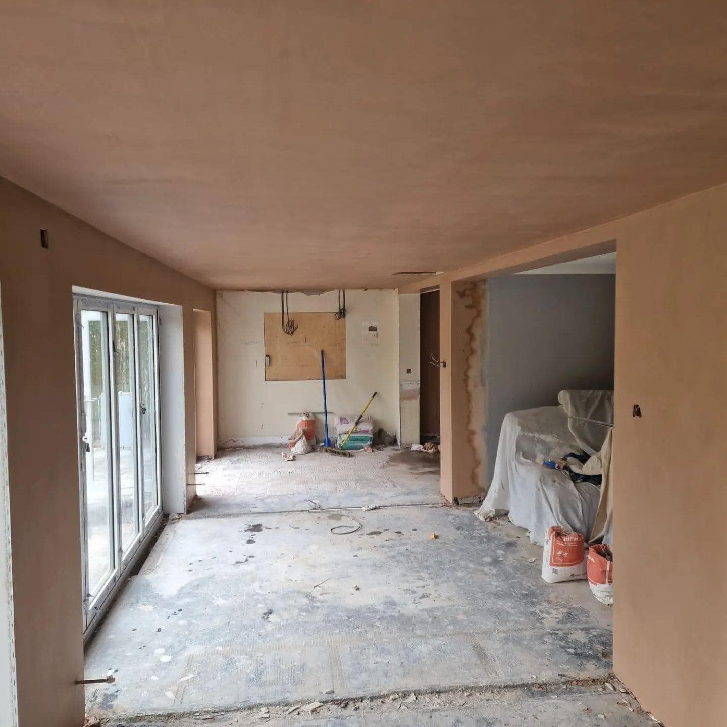 Interior room under construction, with plaster walls and floor. Sliding glass door visible.
