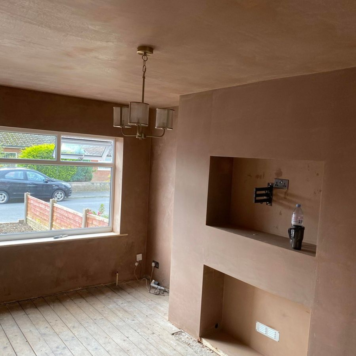Room with fresh plaster walls, a window overlooking a street, and an alcove with a mounted TV bracket.