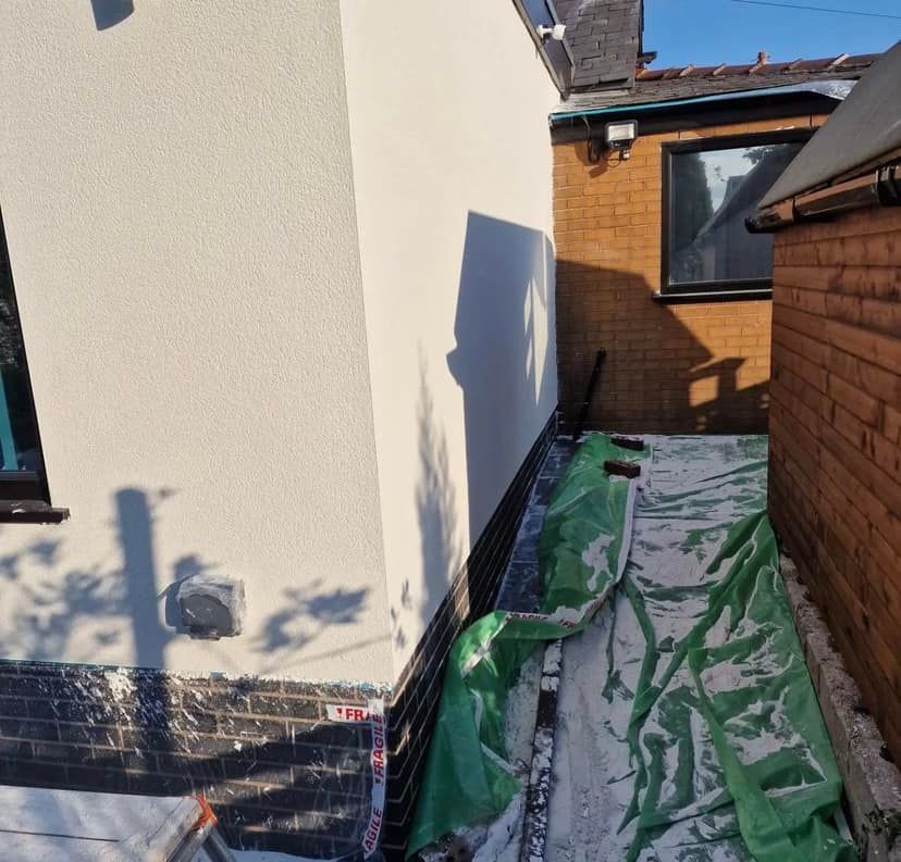 Narrow outdoor space between two buildings, one white stucco, one brick, with tarp and building materials.