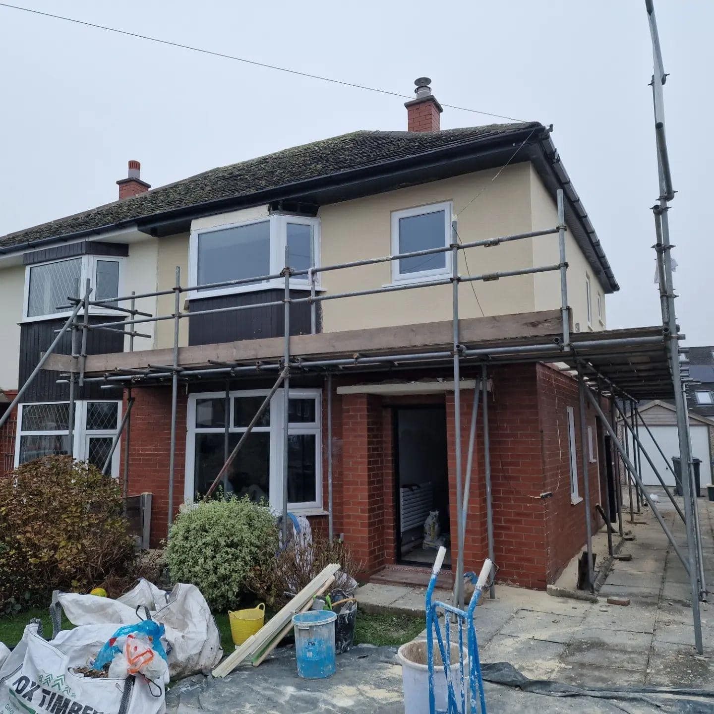 Two-story house with scaffolding, brick and stucco exterior, undergoing renovation.