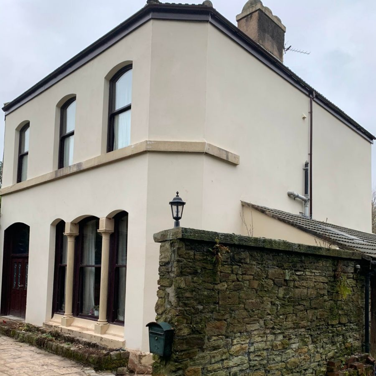 Beige two-story house with arched windows and a stone wall in front.