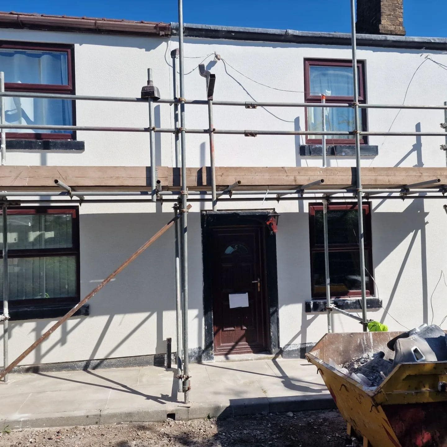 White house with scaffolding; door, windows, and debris container.