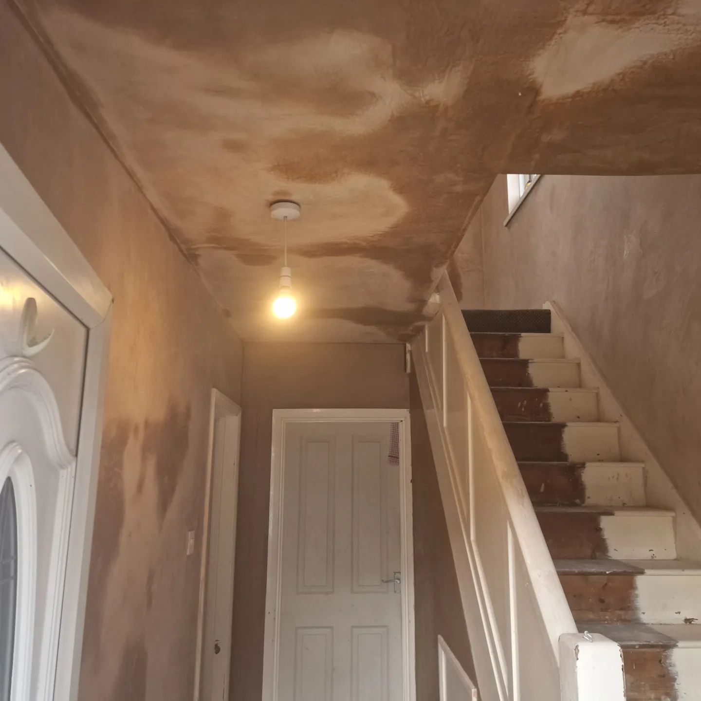 Hallway under renovation with exposed plaster on ceiling, stairs on the right, and a door on the left.