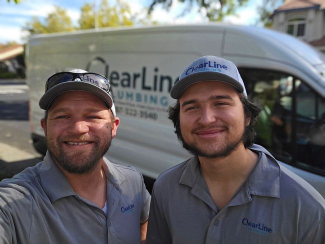 Man in front of a white van with ClearLine Plumbing logo, smiling. Van has a QR code and phone number.