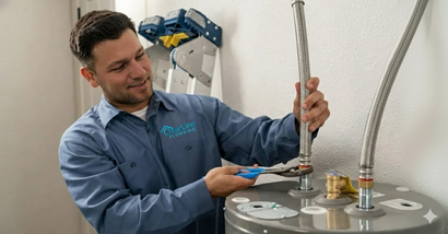 Plumber by a water heater gives a thumbs up in a garage.