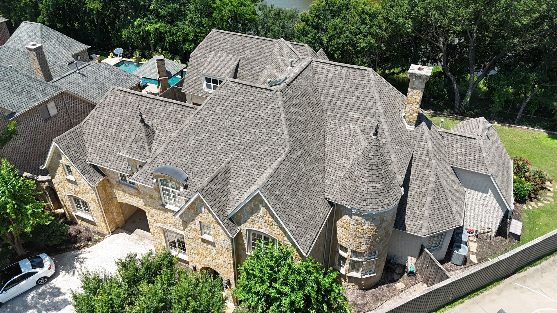 Large stone house with multiple roof sections and chimneys, overlooking greenery.