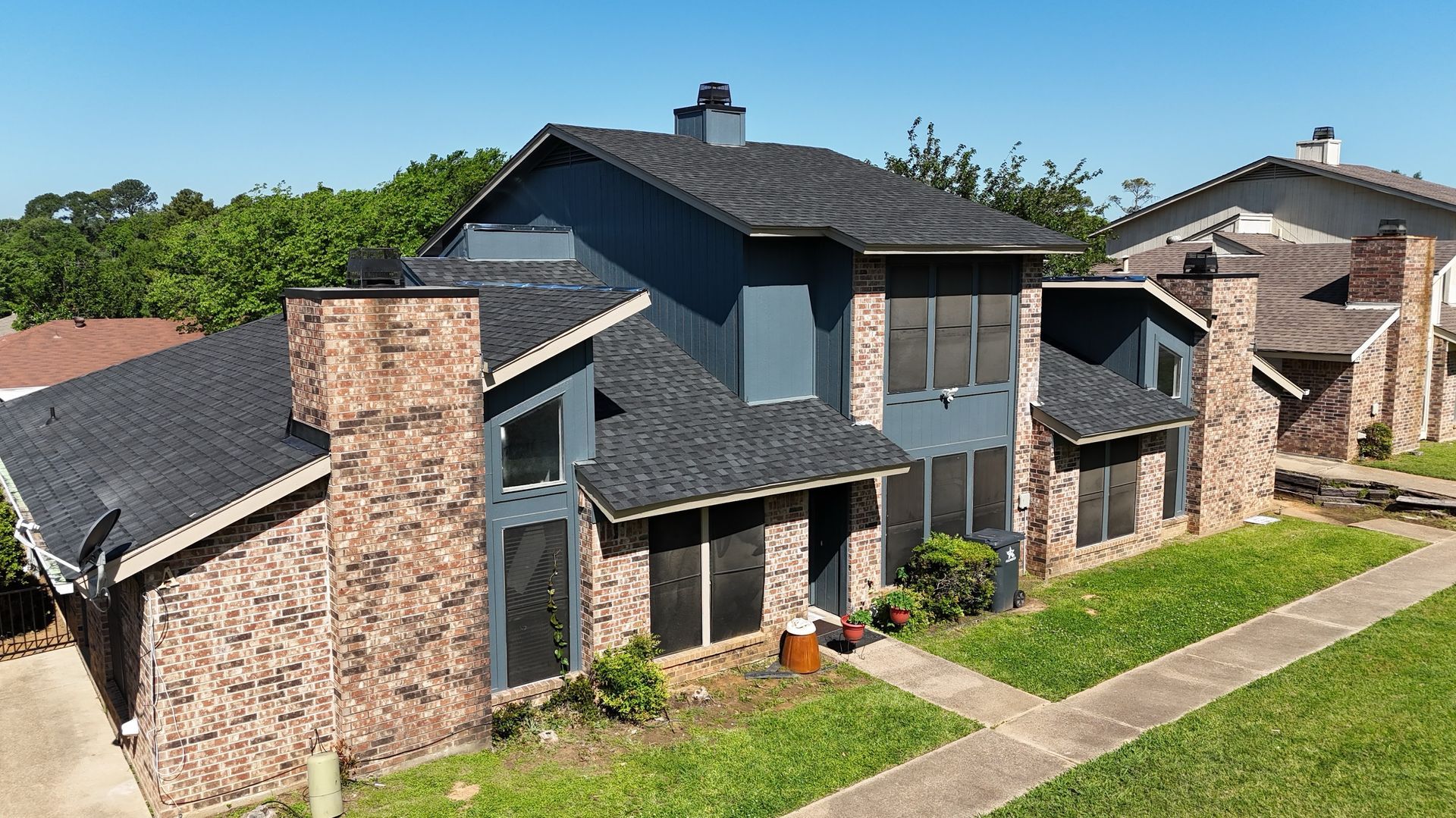 Two-story house with brick exterior and dark blue siding, black shingle roof, green lawn, sunny day.