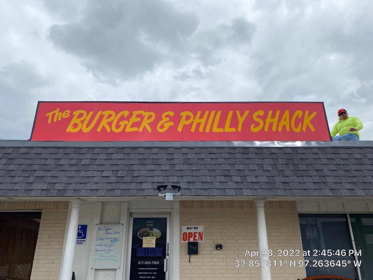 Damaged building: Ruined roof with exposed wooden beams, boarded-up window, white textured wall, and cloudy sky.