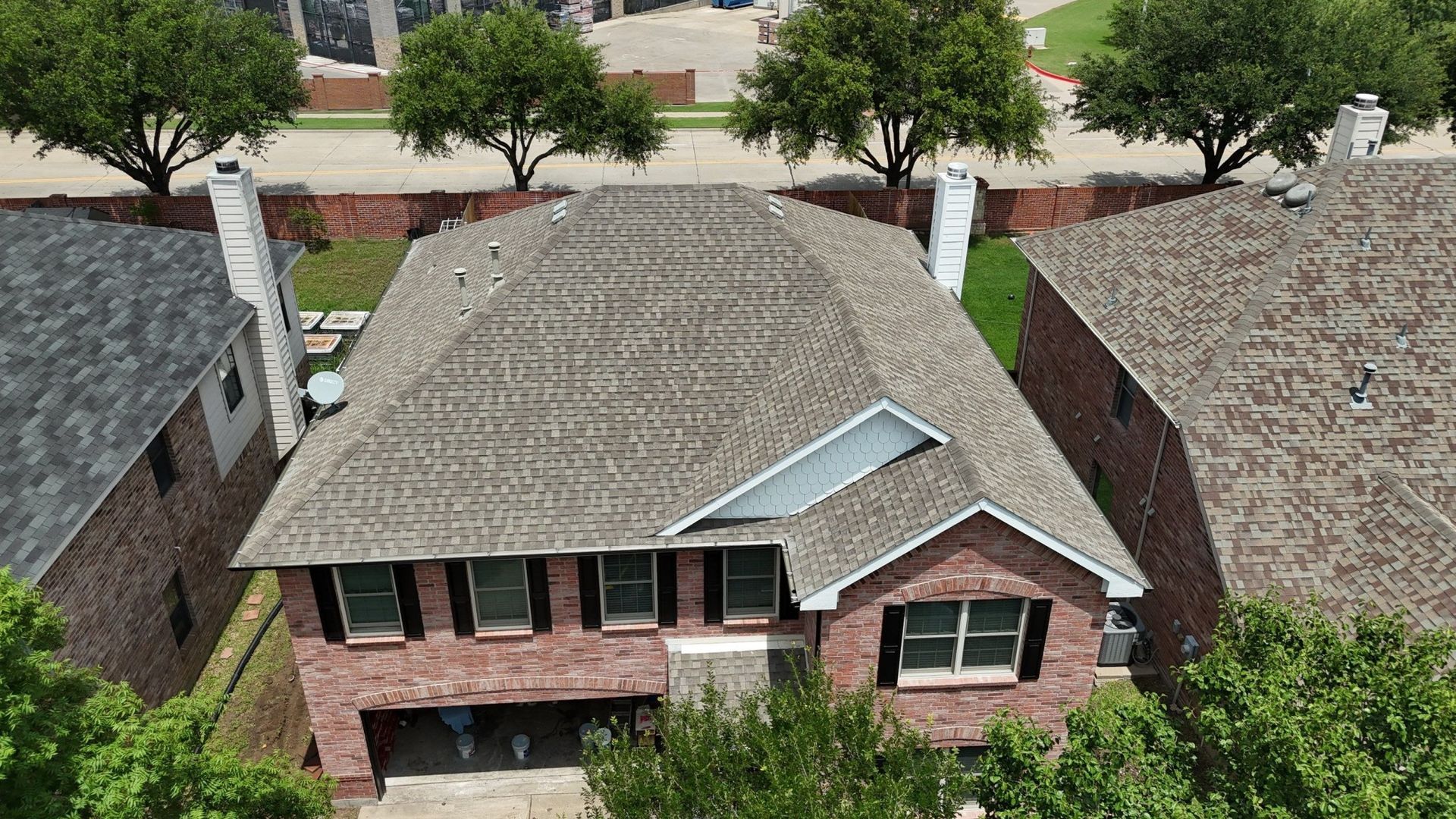 Aerial view of a two-story brick house with a brown roof and surrounding trees in a residential area.