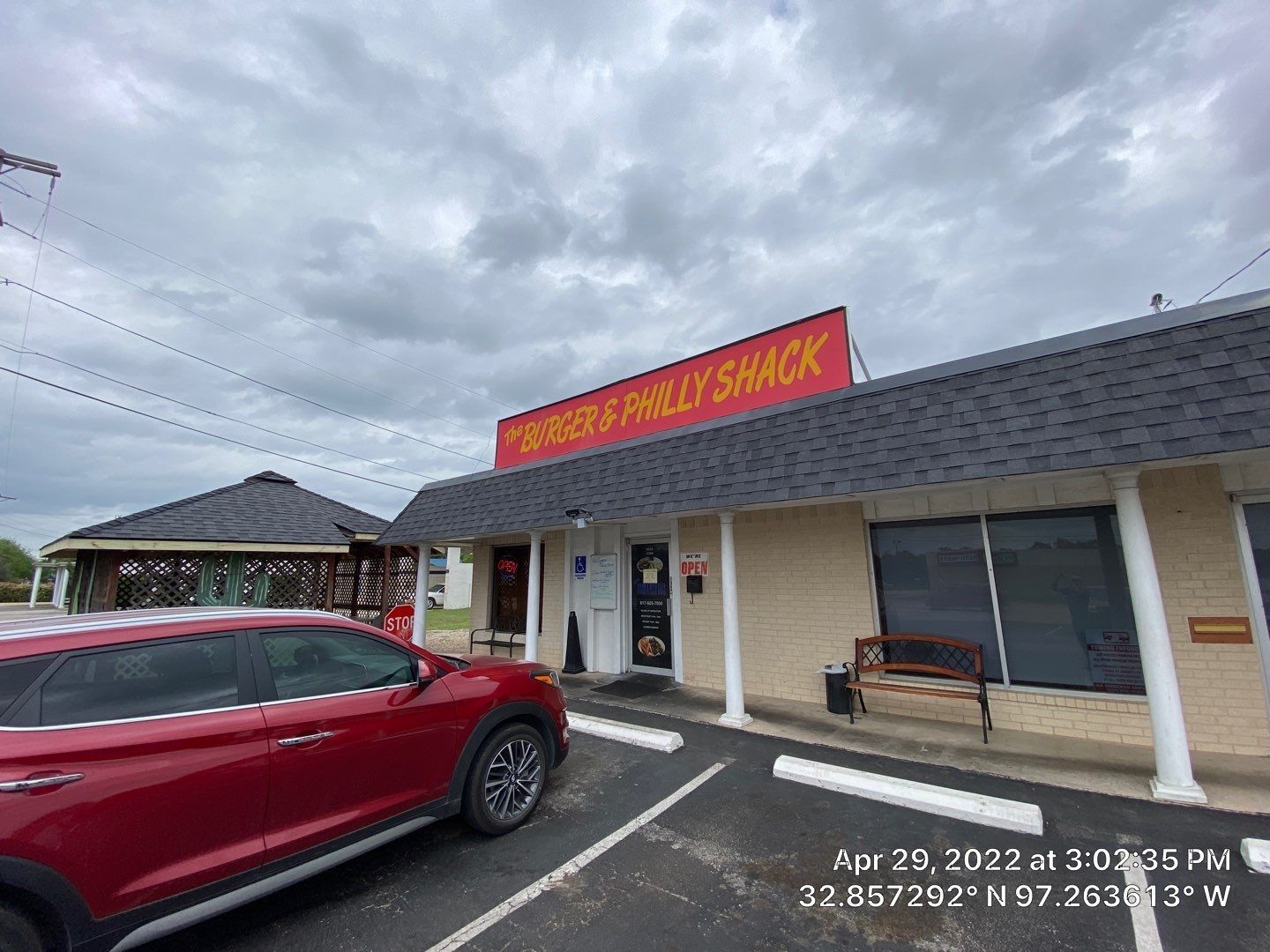 Burger & Philly Shack storefront with red sign, red car parked outside. Cloudy sky.