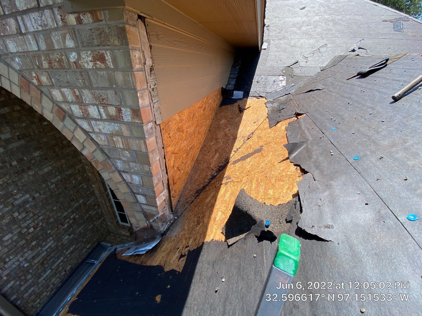 Damaged building: Ruined roof with exposed wooden beams, boarded-up window, white textured wall, and cloudy sky.
