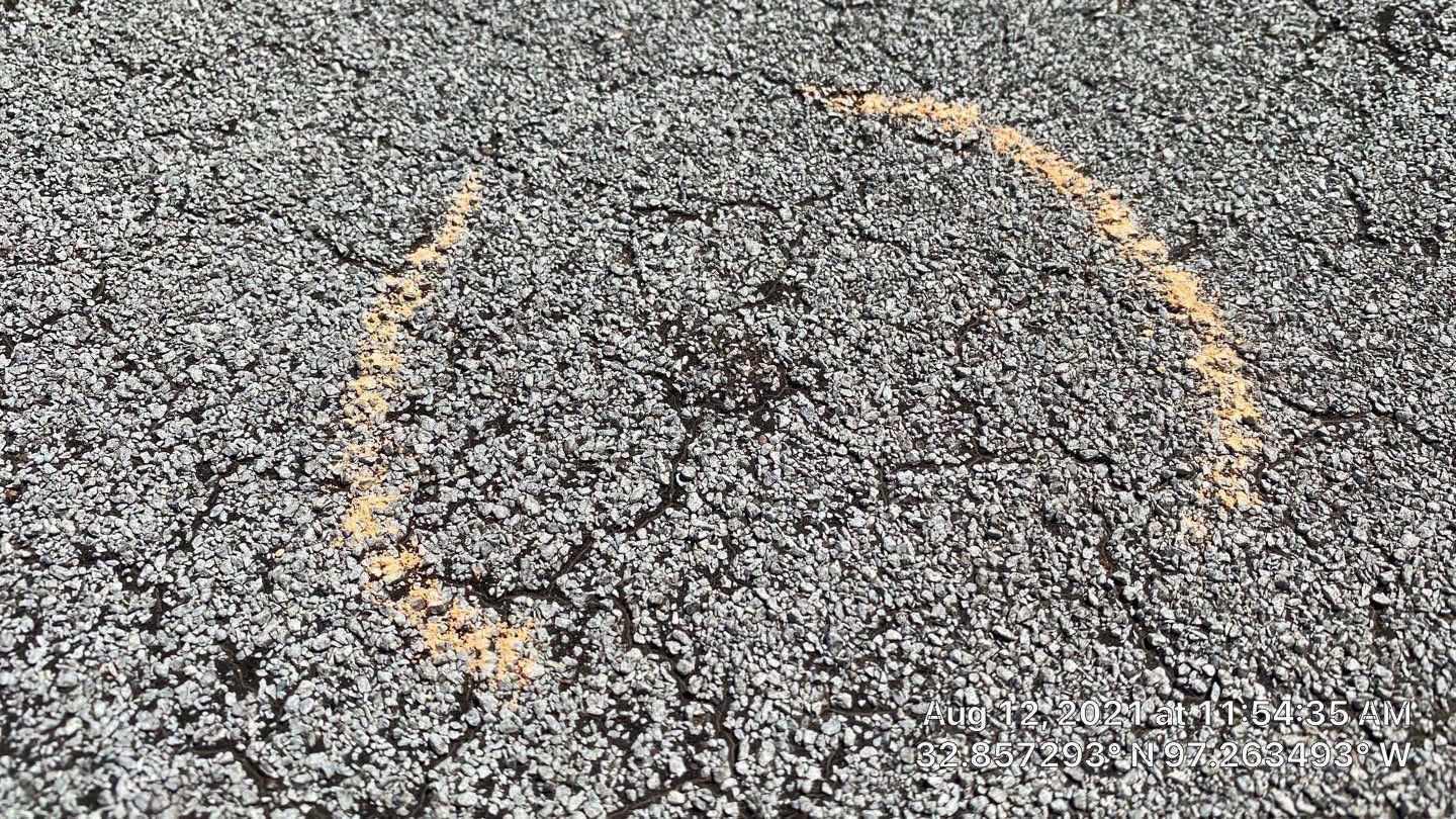 Close-up of asphalt, with a curving, yellow chalk outline on the surface.