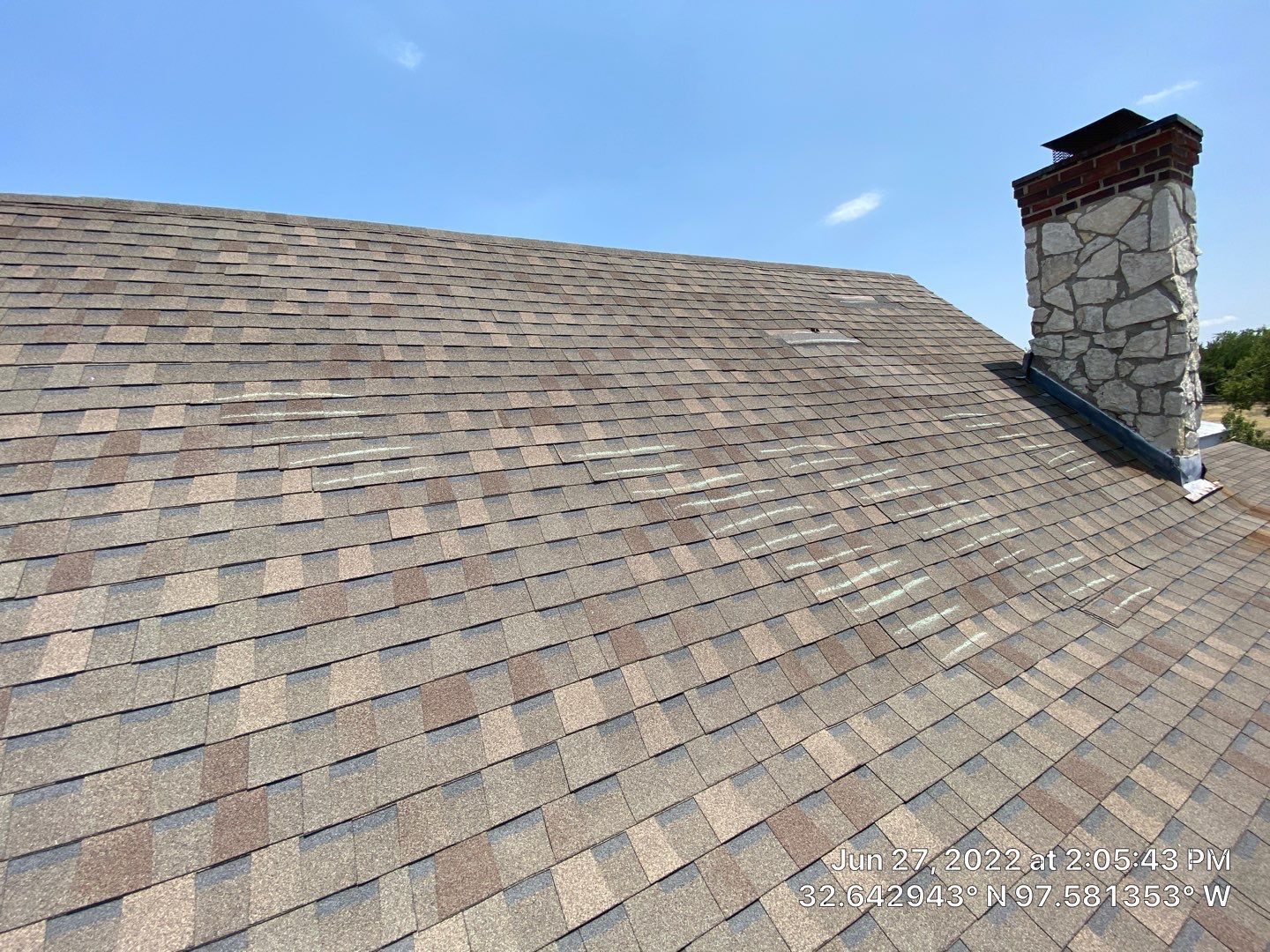 A shingled roof with a stone chimney against a bright blue sky.