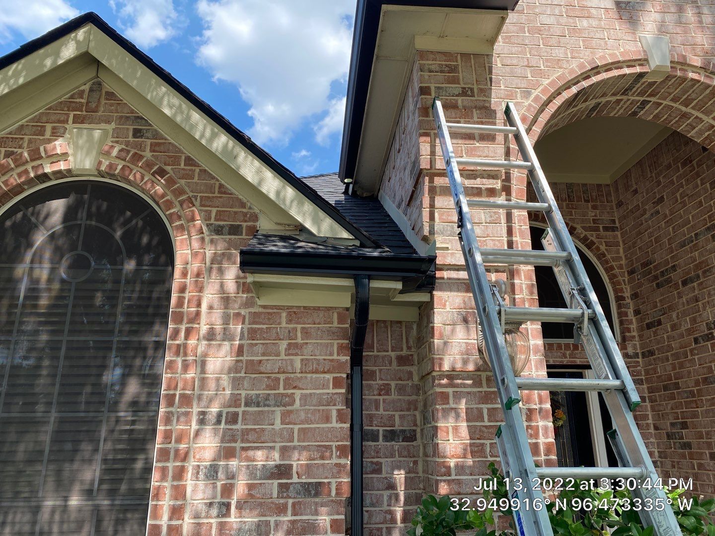 Ladder leaning against a brick building with dark gutters and a roof.