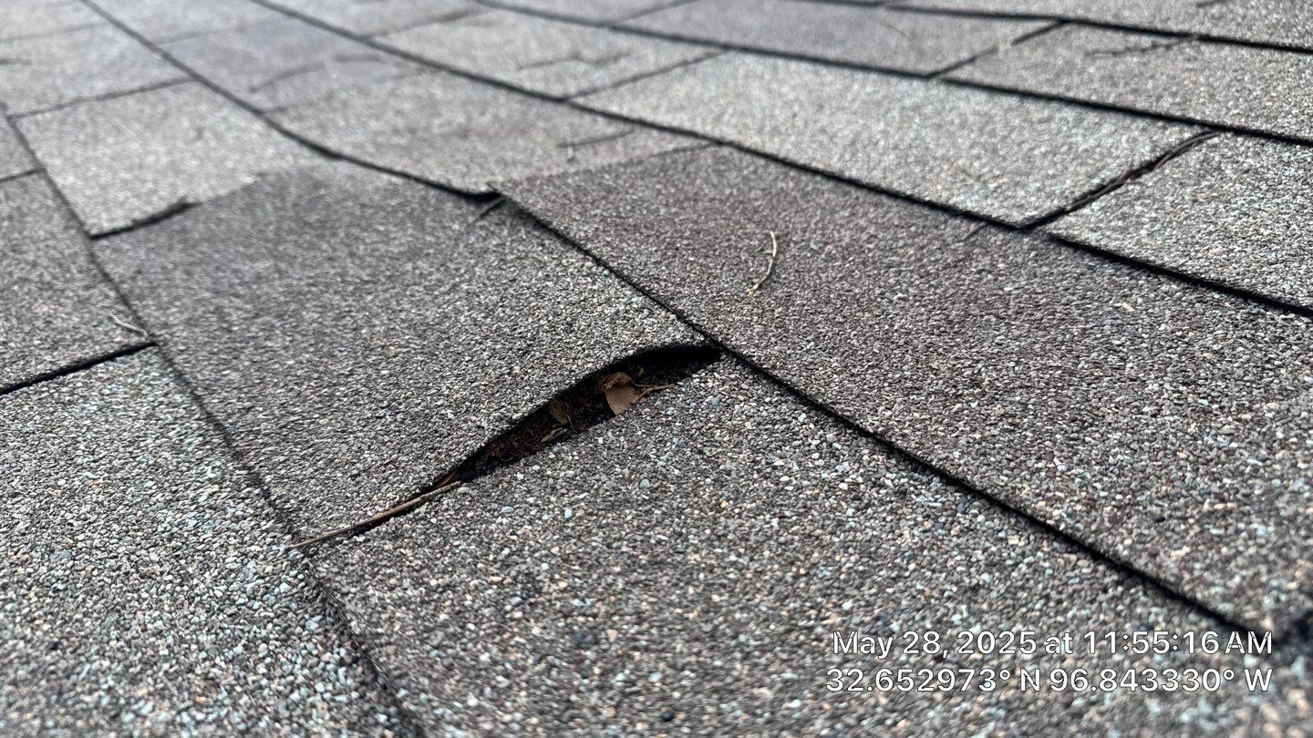 Close-up of asphalt shingles on a roof with a visible crack, weathered gray color.